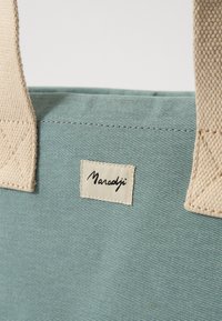 Lyseblå canvas totebag med beige vevde håndtak og et tekstilmerke som viser navnet "Maradji". Har diagonale teksturerte linjer.