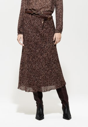 Braunes Maxikleid mit Leopardenmuster aus durchsichtigem Stoff, featuring lange Ärmel und einem gebundenen braunen Gürtel, kombiniert mit schwarzen Knöchelstiefeln.