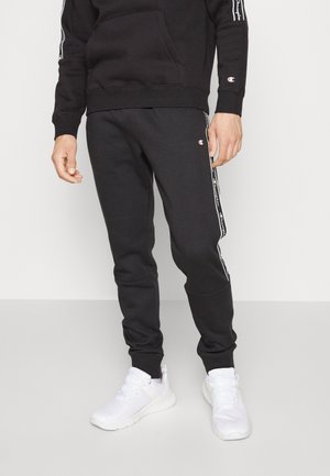 Czarna bluza z kapturem z przednią kieszenią i elastycznymi mankietami, zestawiona z czarnymi dresami z bocznymi pasami i logo, dopełniona białymi trampkami.