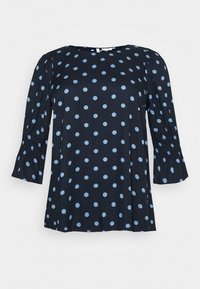 Blouse bleu marine avec des pois bleu clair, dotée de manches bouffantes et de poignets élastiques, fabriquée à partir d'un tissu lisse.