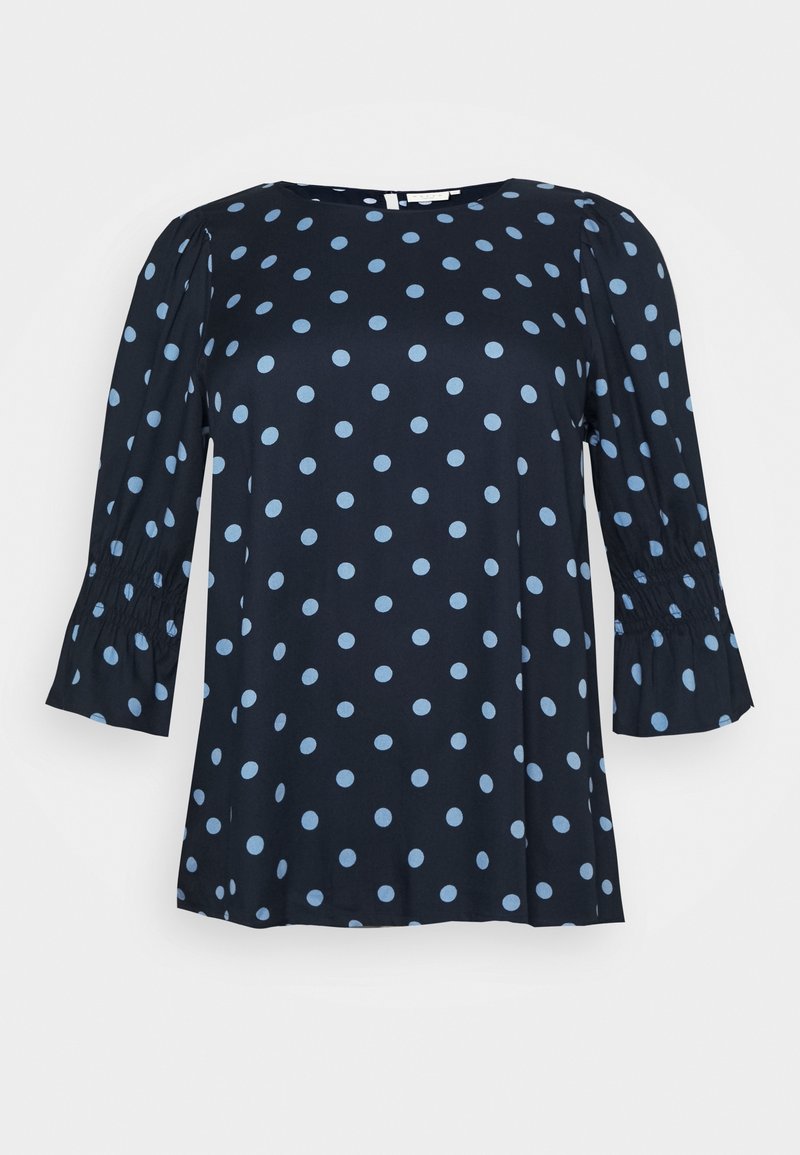 Blouse bleu marine avec des pois bleu clair, dotée de manches bouffantes et de poignets élastiques, fabriquée à partir d'un tissu lisse.