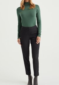 Grön, figurnära polotröja med långa ärmar, tillsammans med svarta strukturerade byxor. Byxorna har knäppning och smal passform.