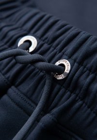 Gros plan sur une ceinture élastique bleu marine avec un cordon passé à travers des œillets métalliques argentés sur un pantalon décontracté.