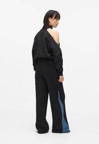 Sudadera negra con diseño de hombro descubierto y pantalones anchos negros que presentan un panel de mezclilla azul a lo largo de la costura exterior. Ajuste casual.