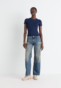T-shirt ajustée à manches courtes navy associée à un pantalon large en denim bleu clair et des baskets beiges ; tissu lisse, design décontracté, minimalisme dans les détails.
