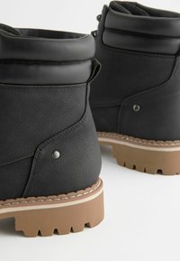 Botas de tobillo de imitación de cuero negro con un acabado texturizado, cuello acolchado y suela de goma con profundas protuberancias para mayor tracción.