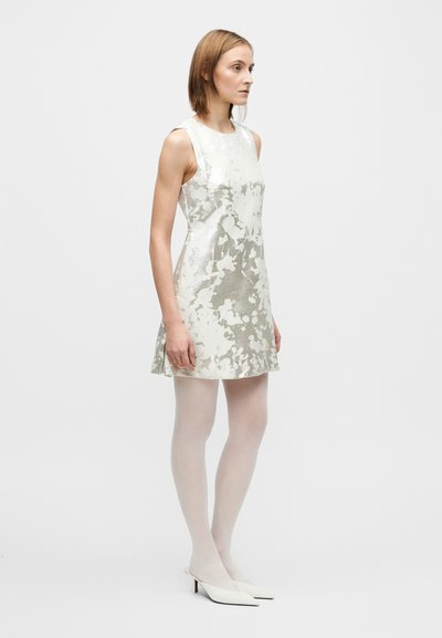 Rochie fără mâneci, de culoare argintiu deschis, cu modele florale, siluetă în linie A, material texturat, combinată cu ciorapi albi și mule ascuțite.