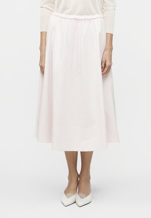 Kvinde iført en hvid midi-nederdel med elastik i taljen og snøre, kombineret med hvide spidse hæle med blonder.