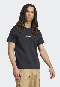 Camiseta de manga corta negra, hecha de material de algodón, con un logo blanco de "TERREX" en el pecho. Textura suave y corte relajado.