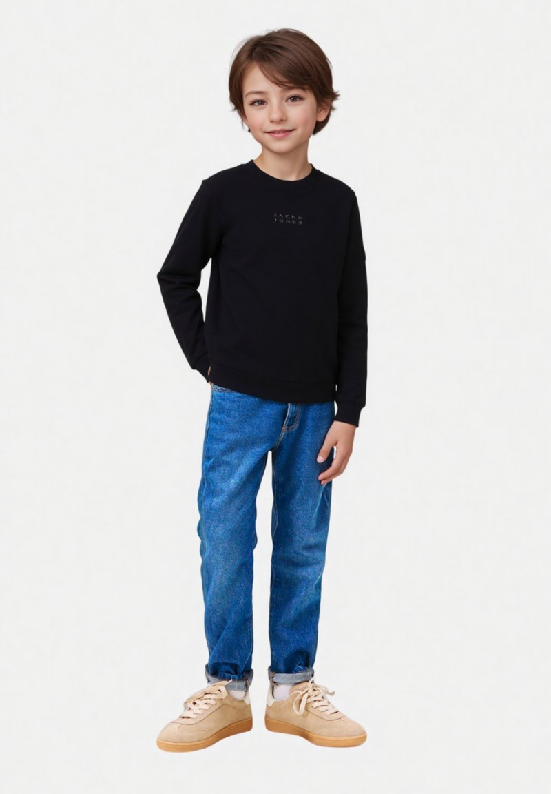 Maglietta nera a maniche lunghe con logo, jeans di denim blu e sneakers beige. Fit casual con taglio dritto e polsini arrotolati sui jeans.