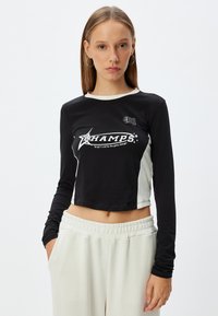 Zwarte lange mouwen cropped shirt met witte accenten, met de tekst "CHAMPS" en sterdetails op de voorkant, gemaakt van een zachte katoenen stofmix.
