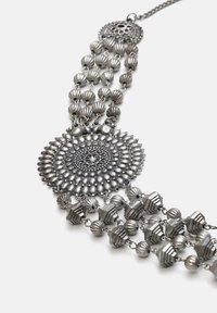 Collana in tonalità argento con complessi design pendenti circolari e geometrici, accenti di perline e catene a strati.