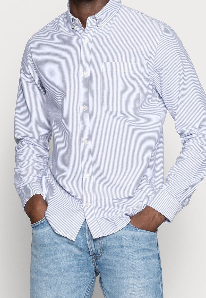 Blå och vit randig skjorta med knappar, krage, långa ärmar och bröstficka, gjord av lätt tyg.