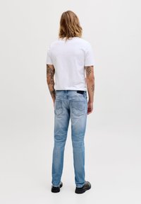 Μπλε τζιν παντελόνι με ξεθωριασμένο φινίρισμα, εφαρμοστή γραμμή και πίσω τσέπες. Συνδυασμένο με απλό λευκό κοντομάνικο μπλουζάκι. Ορατά μαύρα παπούτσια.