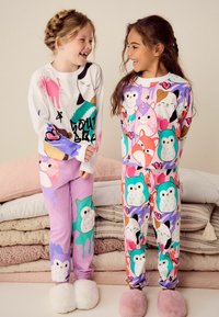 Två barn har på sig färgglada pyjamaser. Det ena barnet har en vit topp med djurmönster och lila byxor. Det andra barnet har en mönstrad topp och byxor med hjärtan och djur.