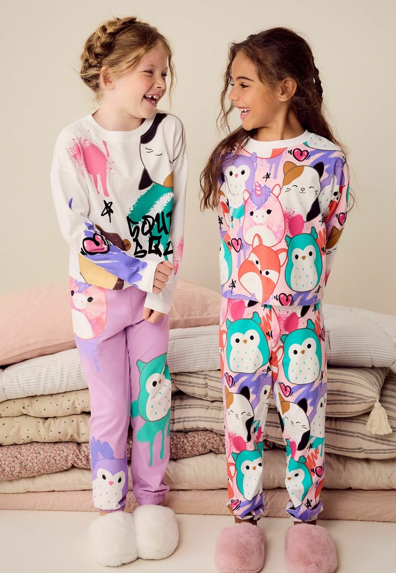 Två barn har på sig färgglada pyjamaser. Det ena barnet har en vit topp med djurmönster och lila byxor. Det andra barnet har en mönstrad topp och byxor med hjärtan och djur.