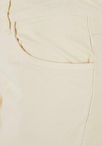 Pantalon en coton beige avec une poche arrondie dotée de coutures visibles et d'une texture douce, mettant en avant une finition lisse et un design simple.