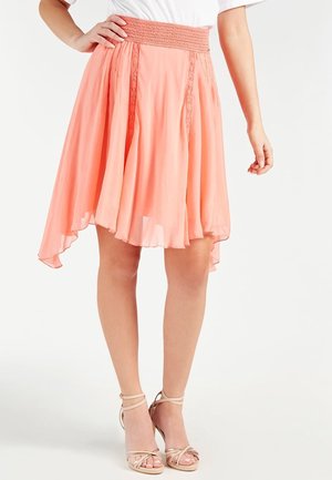 Jupe en chiffon pêche avec une taille smockée, un ourlet asymétrique flottant et des détails en dentelle le long des coutures avant.