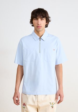 Light blue polo shirt with a zip collar, two front pockets, and short sleeves. Features a small brand logo on the chest.