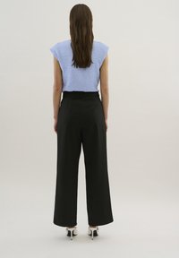 Top court texturé bleu clair avec des manches courtes, associé à un pantalon large noir. Les chaussures présentent des talons blancs avec des accents noirs.