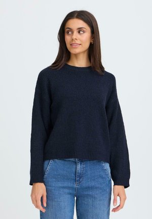 Mørkeblå, ribbet striktrøje med lange ærmer og rund halsudskæring, parret med denimjeans. Teksturen ser blød og tyk ud.