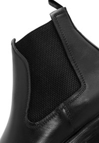 Bota Chelsea de cuero negro con paneles laterales elásticos, que presenta un acabado suave, acentos cosidos y un inserto de tela texturizada en la parte superior.