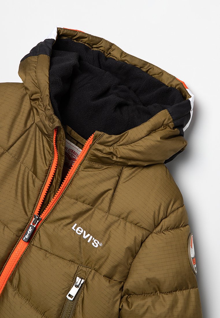Doudoune vert olive avec capuche en polaire noire, fermeture éclair orange et logo blanc. Présente une texture matelassée et un détail de patch.