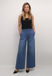 Breda blå denimbyxor med en slät textur, hög midja och klassisk femfickdesign, som kombineras med en svart åtsittande linne.