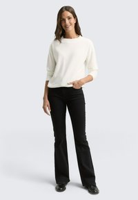 Haut blanc à manches longues en côte avec un col rond, associé à un jean noir évasé. La tenue présente une coupe décontractée et un design minimaliste.