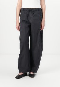 Black, loose-fitting trousers with an elastic waistband and drawstring. Made of smooth fabric with side pockets and a relaxed silhouette.