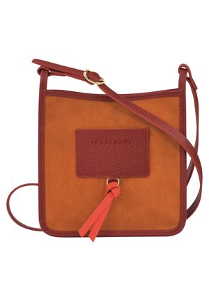 Brązowa torba na ramię z zamszu i skóry, z regulowanym paskiem, przednią skórzaną naszywką i dekoracyjnymi czerwonymi skórzanymi frędzlami.