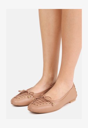 Blote benen met lichtbruine leren ballerina's met decoratieve veters en kleine metalen studs op de hiel.