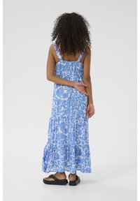 Maxikleid in Hellblau mit floralem Muster; mit verstellbaren Trägern, gerafftem Rücken und gestuftem Rock. Getragen mit schwarzen Sandalen.