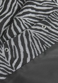 Juodai balta zebro rašto medžiaga su tekstūru, lydima lygaus juodo skyriaus ir dekoratyvine metaline spaudės. 