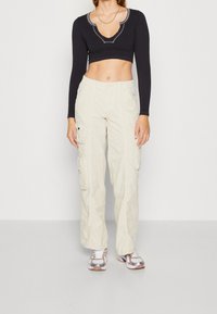 Černý dlouhý rukáv cropped top s hlubokým výstřihem do V a dekorativním prošíváním, spárovaný s béžovými cargo kalhotami s bočními kapsami a uvolněným střihem.