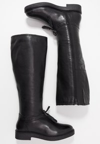 Bottes hautes en cuir noir avec une texture lisse, une fermeture éclair latérale et des coutures décoratives. Comprend un talon bas profilé et un détail en forme de nœud.