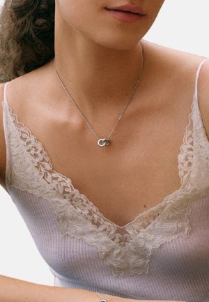 Silver necklace with interlocking loops on a model; she wears a light pink ribbed top with delicate lace trim.