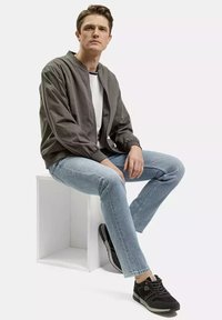 Szara kurtka bomber, biała koszulka, jasnoniebieskie dżinsy i czarne trampki. Kurtka ma ściągaczowy kołnierz i elastyczne mankiety.