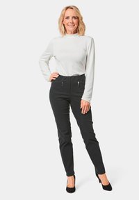 Zwarte aangesloten broeken met een hoge taille, voorzien van twee voorste ritszakken. Gepaarde met een licht top met lange mouwen. Vlotte textuur en een elegante uitstraling.