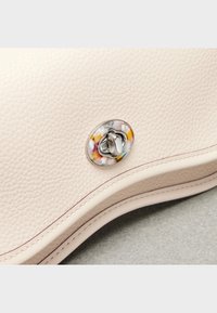 Jasnobeżowa skórzana torebka o teksturowanej powierzchni, wyposażona w metalowe zapięcie z kolorowymi akcentami oraz kontrastujące przeszycia wzdłuż krawędzi.