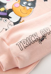 Różowy sweter z postaciami z kreskówek i napisem "TRICK OR TREAT" haftowanym na rękawie, z fakturą dzianiny i detalami na mankietach.