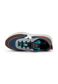 Zapatilla deportiva con un upper en azul y gris, detalles en ante marrón, cordones en azul petróleo y un logo blanco. Cuenta con una gruesa entresuela blanca y una lengüeta en el talón de color rojo.