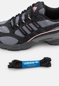 Zwarte en grijze sportschoen met gaas panelen, roze accenten en drie zwarte strepen. Inclusief een zwart-witte gespikkelde veters met een blauwe label.