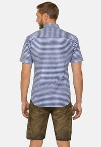 Kurzausgelänges kariertes Hemd in Blau und Weiß, mit geradem Schnitt und Button-down-Kragen, kombiniert mit braunen Shorts.