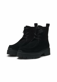 Bocanci negri din suede, cu talpă groasă din cauciuc negru, vârf rotund, cusături contrastante și etichetă cu logo pe lateral. Design cu șireturi.