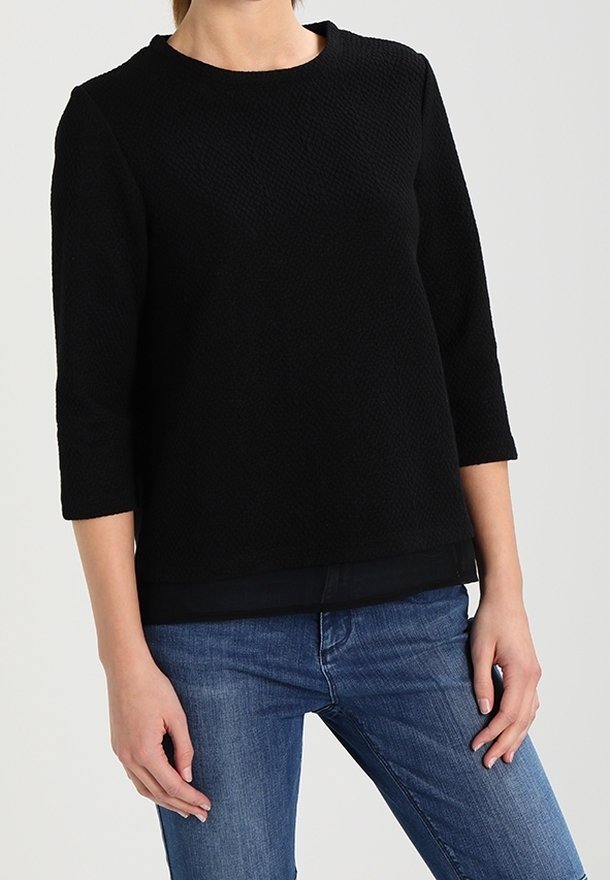 Sort tekstureret sweater med rund hals, trekvartærmer og lige kant, parret med blå jeans.