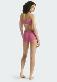 Růžová bavlněná sportovní podprsenka a kraťasy se zdůrazněnými bílými lemy. Pohled zezadu ukazuje zkrácený střih a nastavitelné ramínka. Hladká textura.