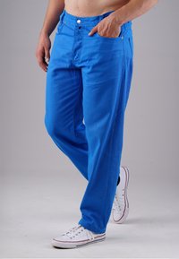 Helle blaue Baumwollhosen mit lässiger Passform, mit einem Knopf- und Reißverschluss, Gürtelschlaufen und seitlichen Taschen. Getragen mit weißen Sneakers.
