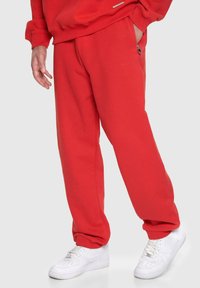 Røde svedderbukser lavet af glat stof, med en afslappet pasform, sidelommer og diskret branding, parret med hvide sneakers.