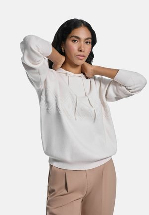 Jasnoróżowa hoodie z teksturowanym wzorem diamentów, wykonana z miękkiego materiału, z prążkowanymi mankietami i sznurkiem; połączona z beżowymi spodniami.